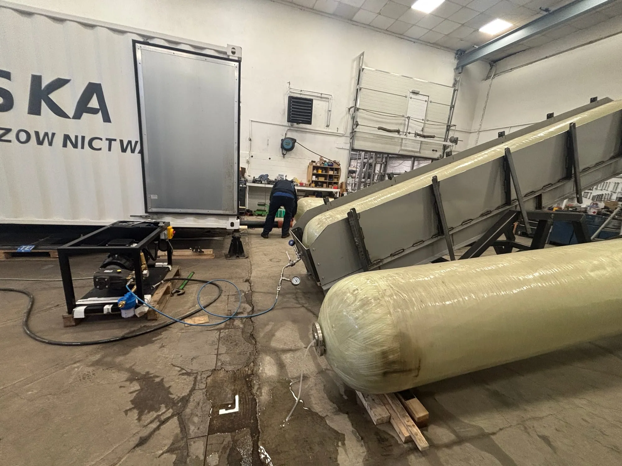 Trwa próba ciśnienia hydraulicznego na cylindrze w warsztacie Gaznet, pompa i manometr podłączone, z tyłu kontener klienta